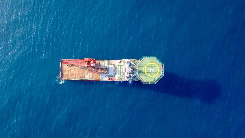 Aerial footage of a Medium size red Offshore supply ship with a Helipad and a large crane