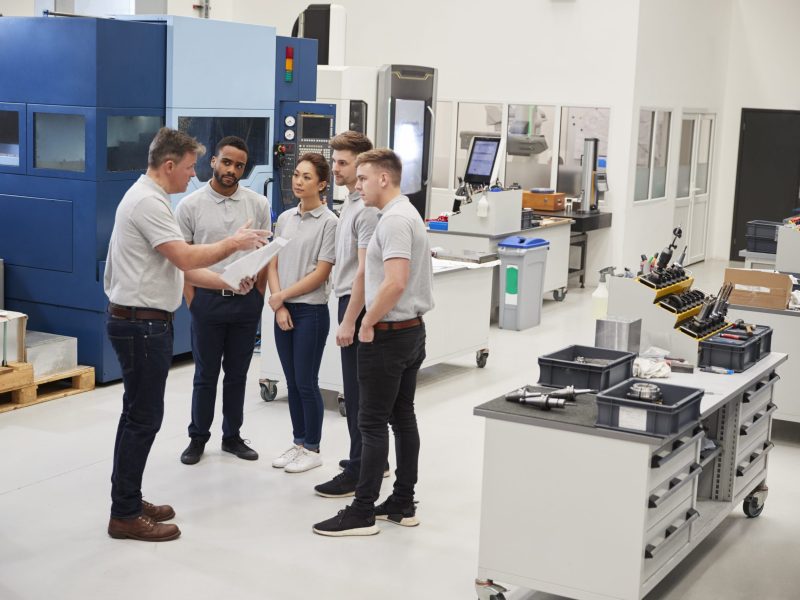 engineering-team-meeting-on-factory-floor-of-busy-37EK6PJ-scaled-1.jpg